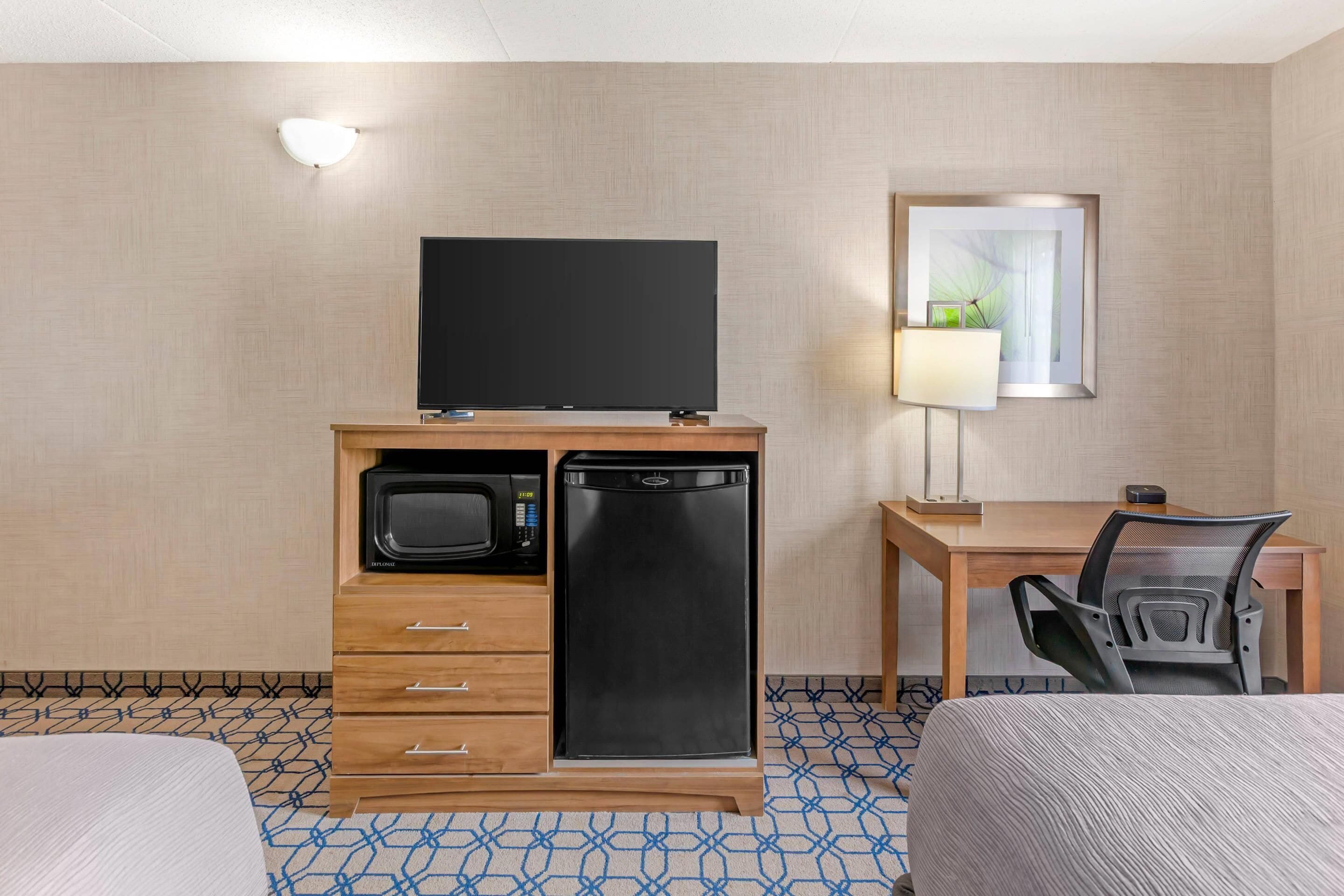 A hotel room with a bed, a desk with a chair, a television, a microwave, and a refrigerator.