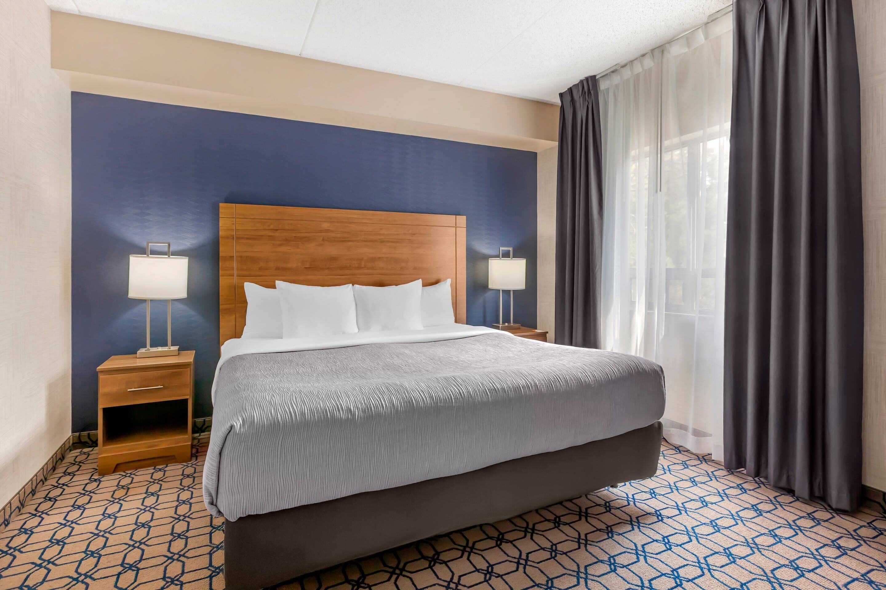 Habitación de hotel con una cama grande, dos mesitas de noche con lámparas, un cabecero de madera y un suelo con diseño.