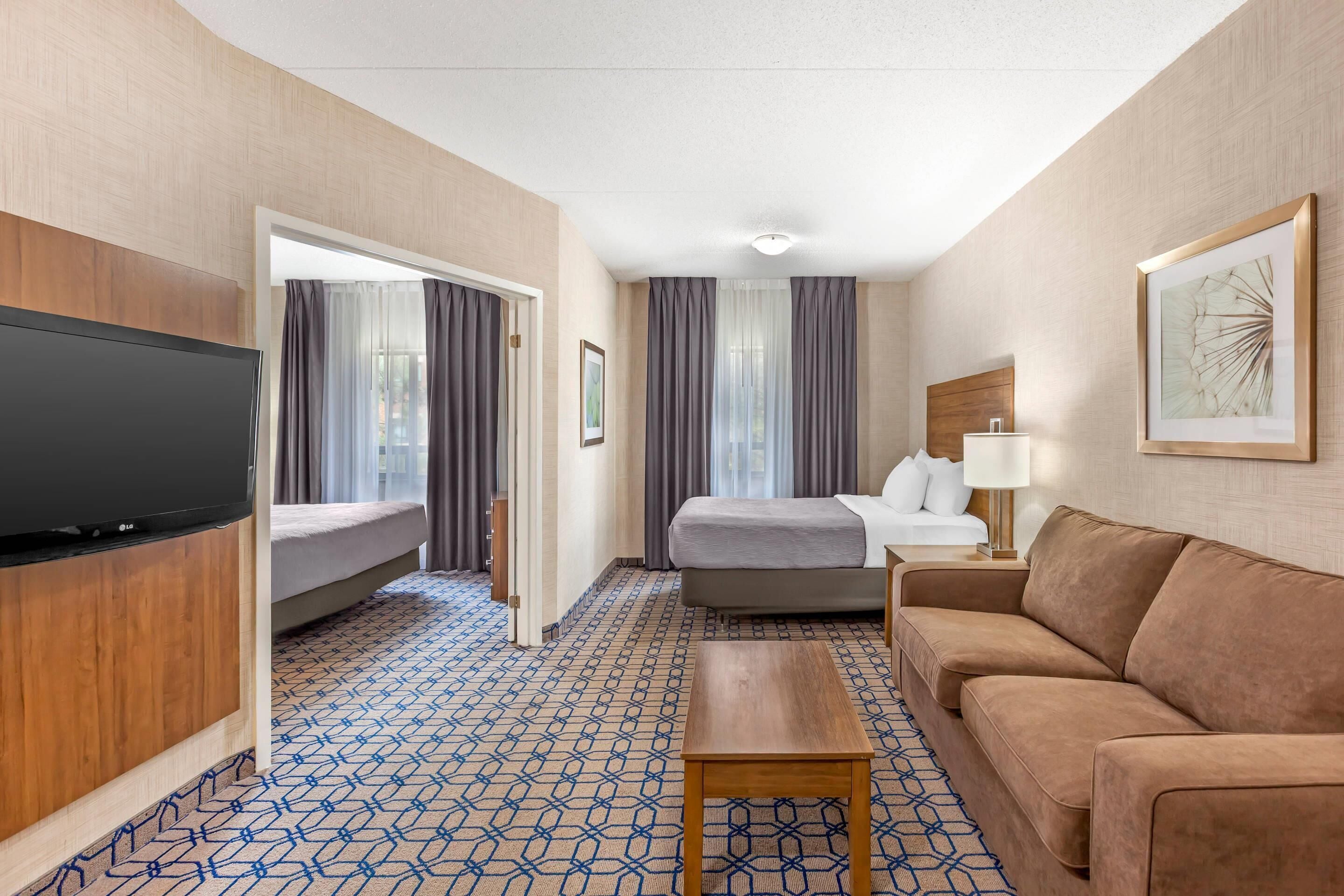 Habitación de hotel con televisión, cama, sofá, mesa de centro y alfombra estampada.