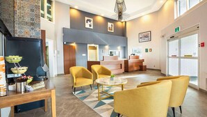 A modern lobby with a reception desk, yellow armchairs, a coffee station, and a patterned rug. - Quality Suites Whitby (Whitby)