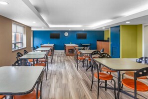 Un comedor con varias mesas y sillas, un reloj en la pared y una ventana con persianas.