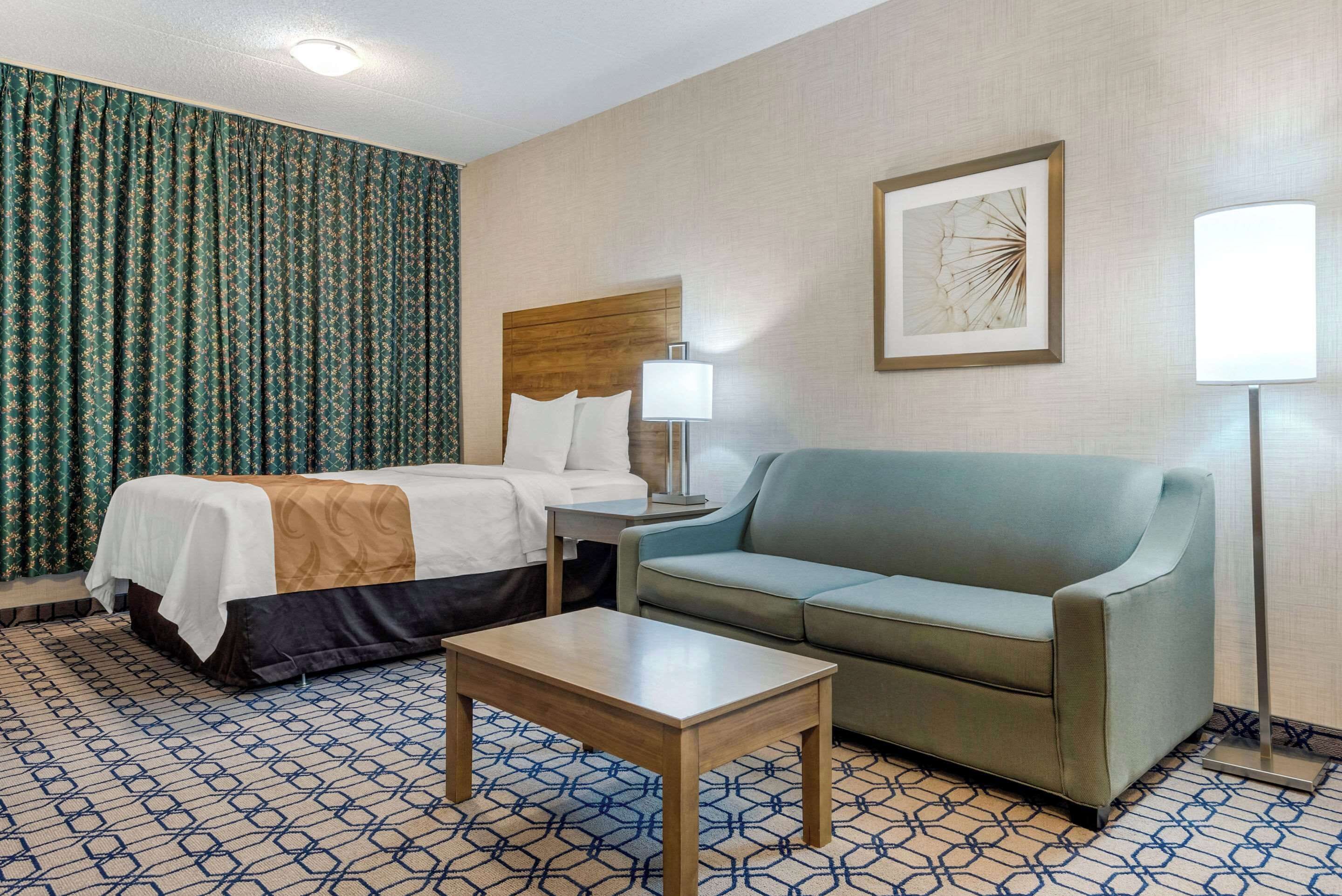 Una habitación de hotel con una cama, un sofá, una mesita y una lámpara.