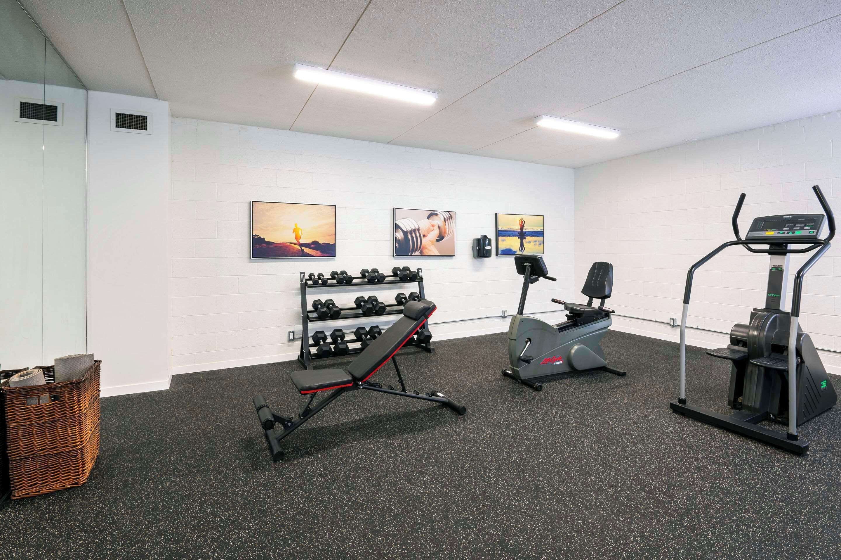 A gym with exercise equipment, a wall-mounted dumbbell rack, and motivational artwork.