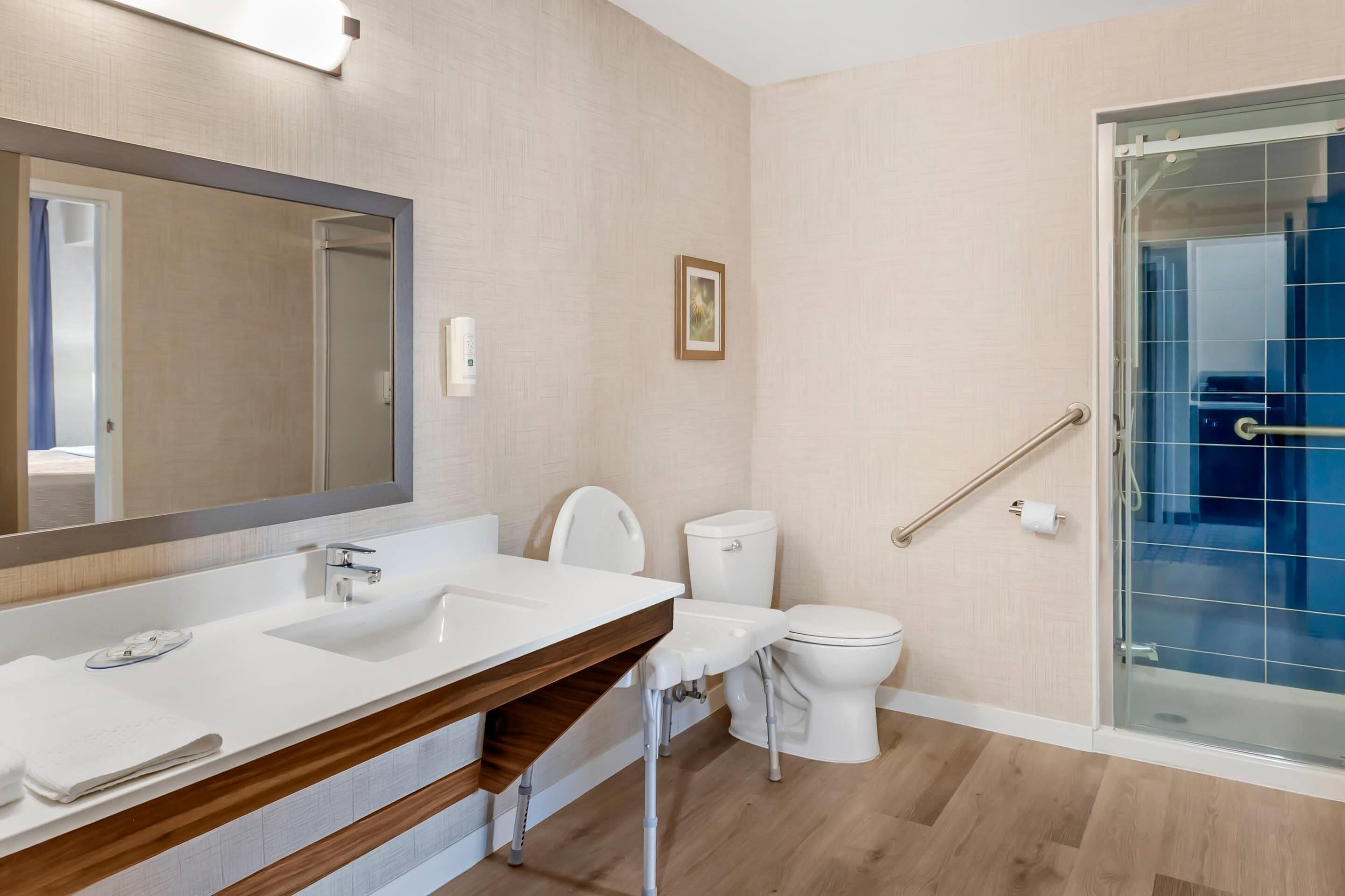 A modern bathroom with a white sink, mirror, and toilet. There is a glass shower enclosure with a blue curtain.