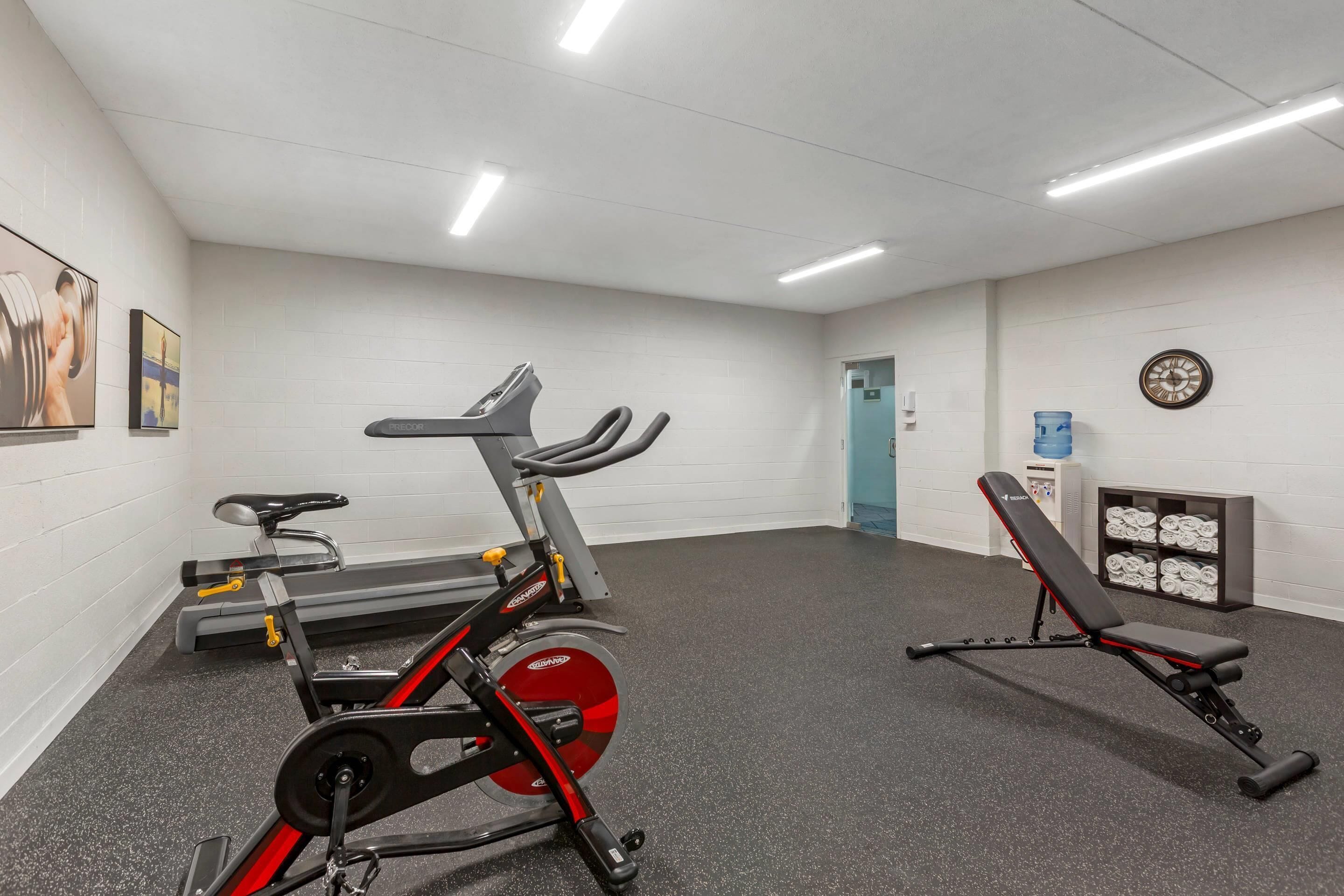 A gym with cardio equipment, a bench, and a water dispenser.