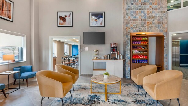 A modern lobby with a round table, comfortable seating, a TV, and a patterned wall. - Quality Suites Whitby (Whitby)