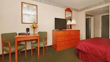 A hotel room with a bed, a desk with a chair, a television, a dresser, and a framed picture on the wall.