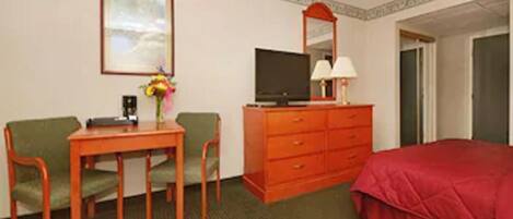 A hotel room with a bed, a desk with a chair, a television, a dresser, and a framed picture on the wall.