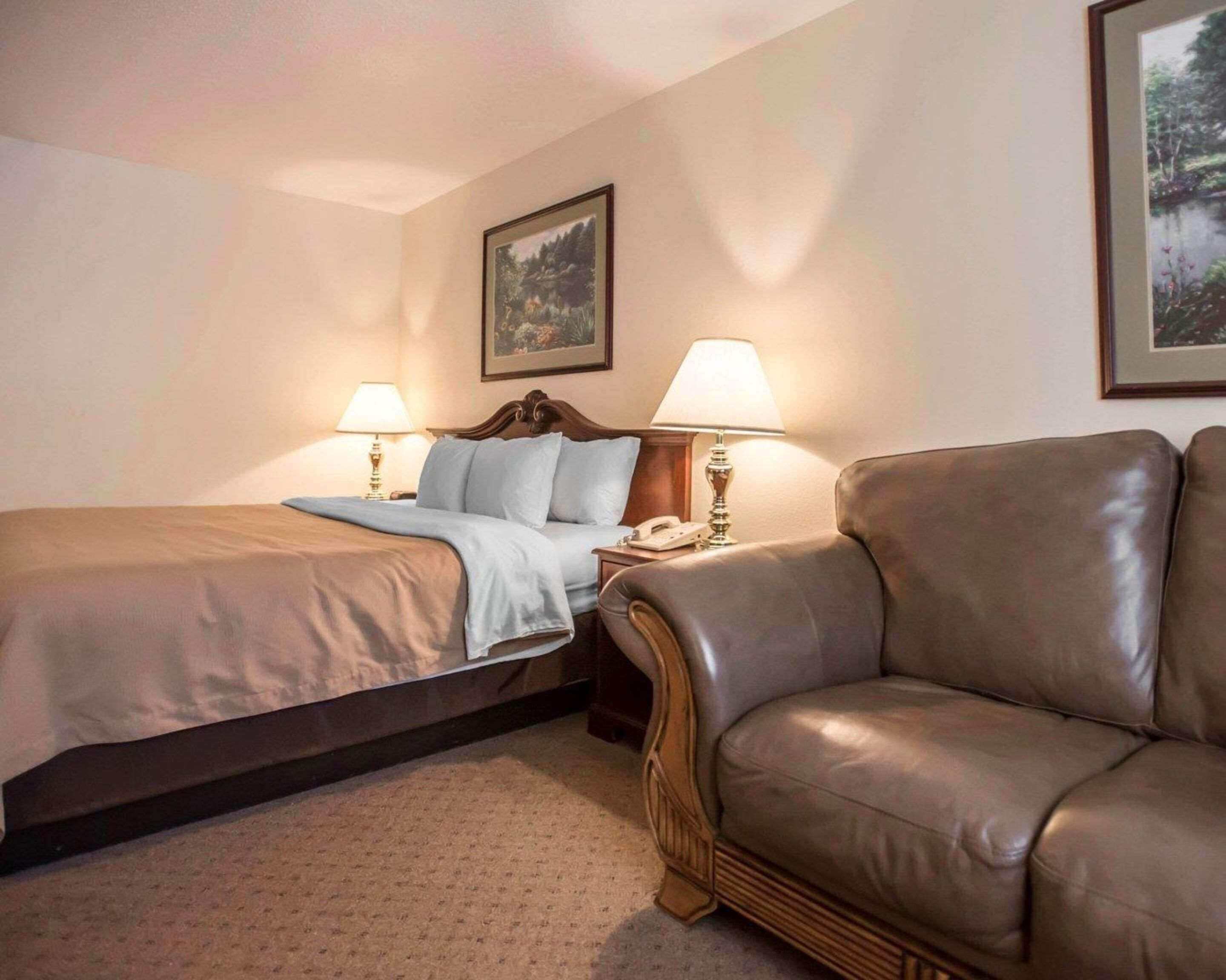 A hotel room with a bed, two bedside lamps, a telephone, a brown leather sofa, and two framed pictures on the wall.