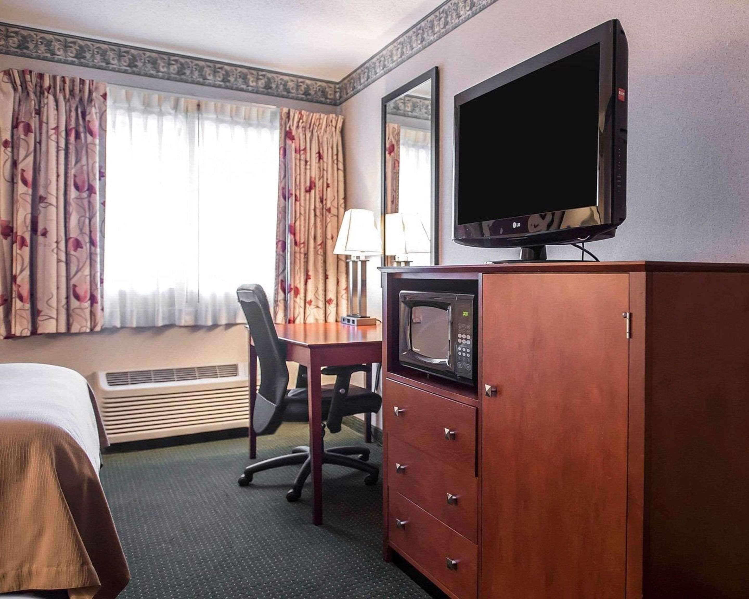 A hotel room with a bed, a desk with a chair, a television, a microwave, and a wardrobe.