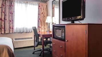 Habitación de hotel con cama, escritorio, silla, televisor, microondas y armario.