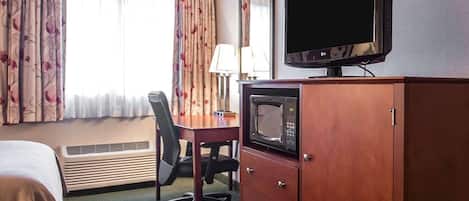 A hotel room with a bed, a desk with a chair, a television, a microwave, and a wardrobe.