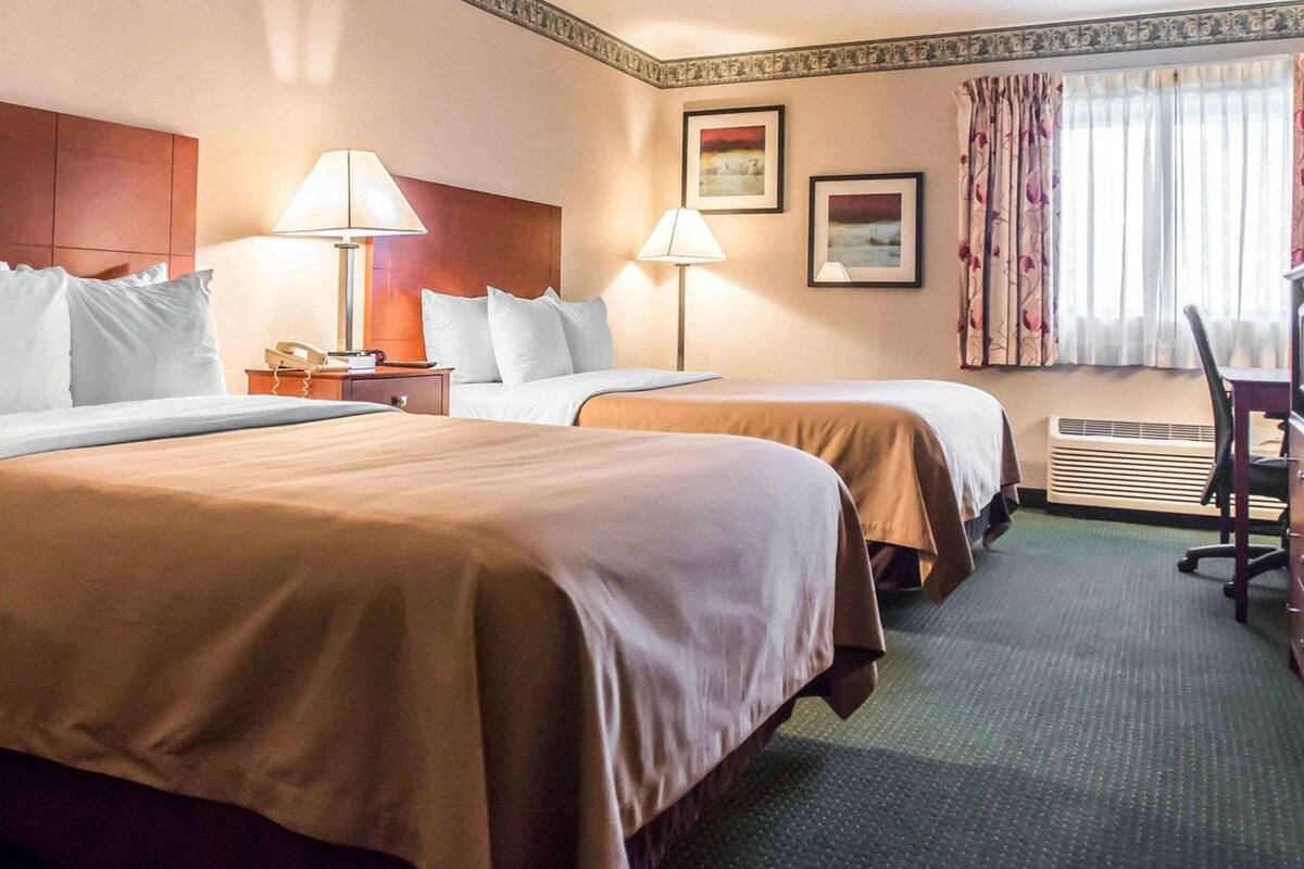 Ein Hotelzimmer mit zwei Betten, einem Schreibtisch, einem Sessel, einem Telefon und einem Fenster mit Vorhängen.