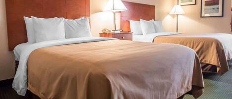 Habitación de hotel con dos camas, cada una con ropa blanca y cabeceros marrones. Hay dos lámparas de noche, un teléfono y cuadros en la pared.