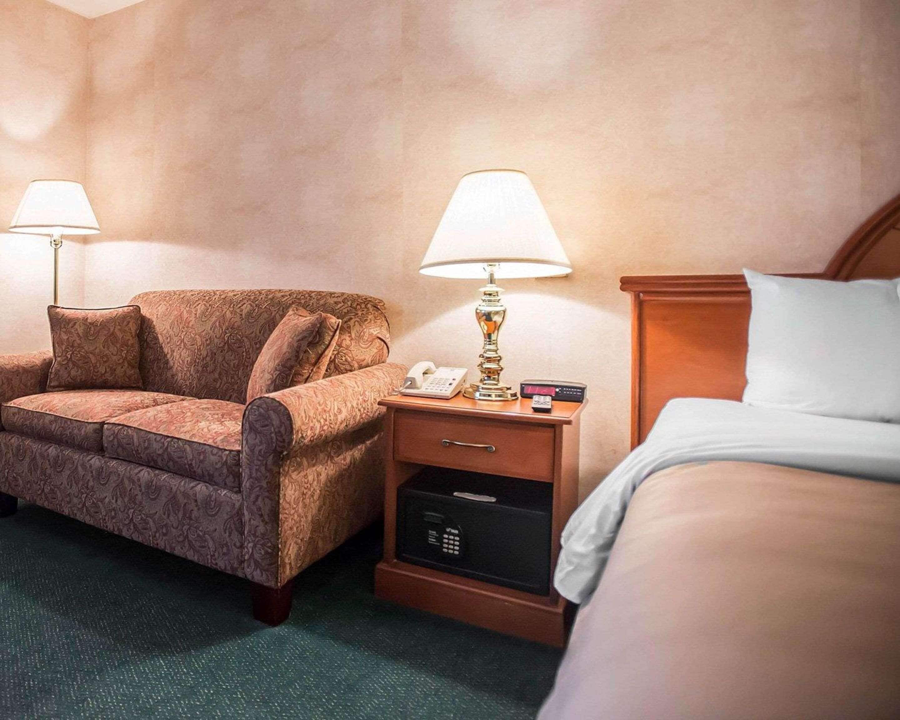 Ett hotellrum med en säng, en soffa, ett nattduksbord med en lampa, en telefon och ett värdeskåp.