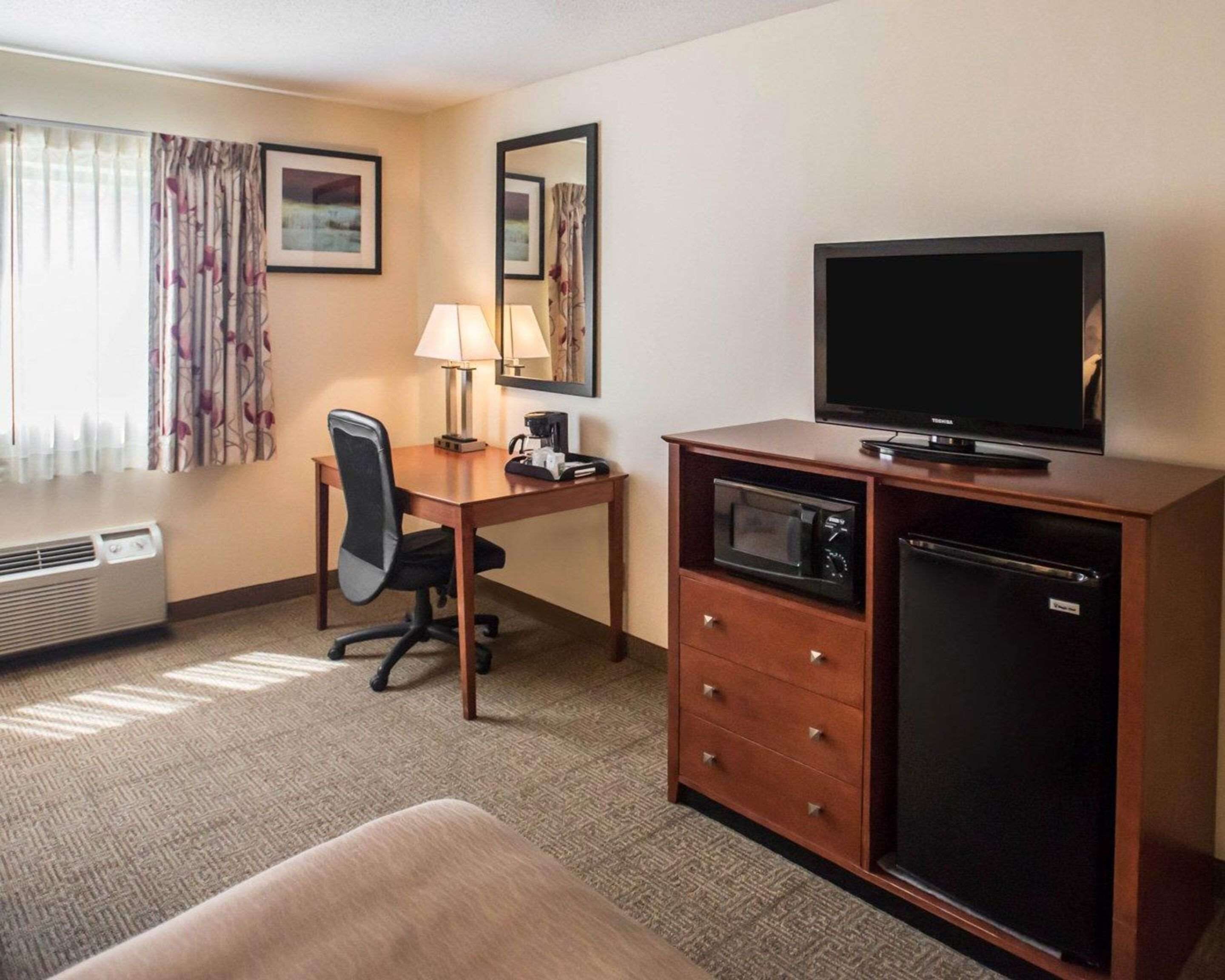 A hotel room with a desk, chair, television, microwave, and a mini-fridge.