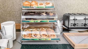 A bakery display with various baked goods in clear containers, a toaster, and kitchen utensils on a countertop.