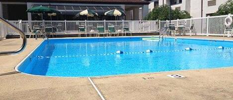 A rectangular pool with clear blue water, surrounded by a white fence and a concrete deck.