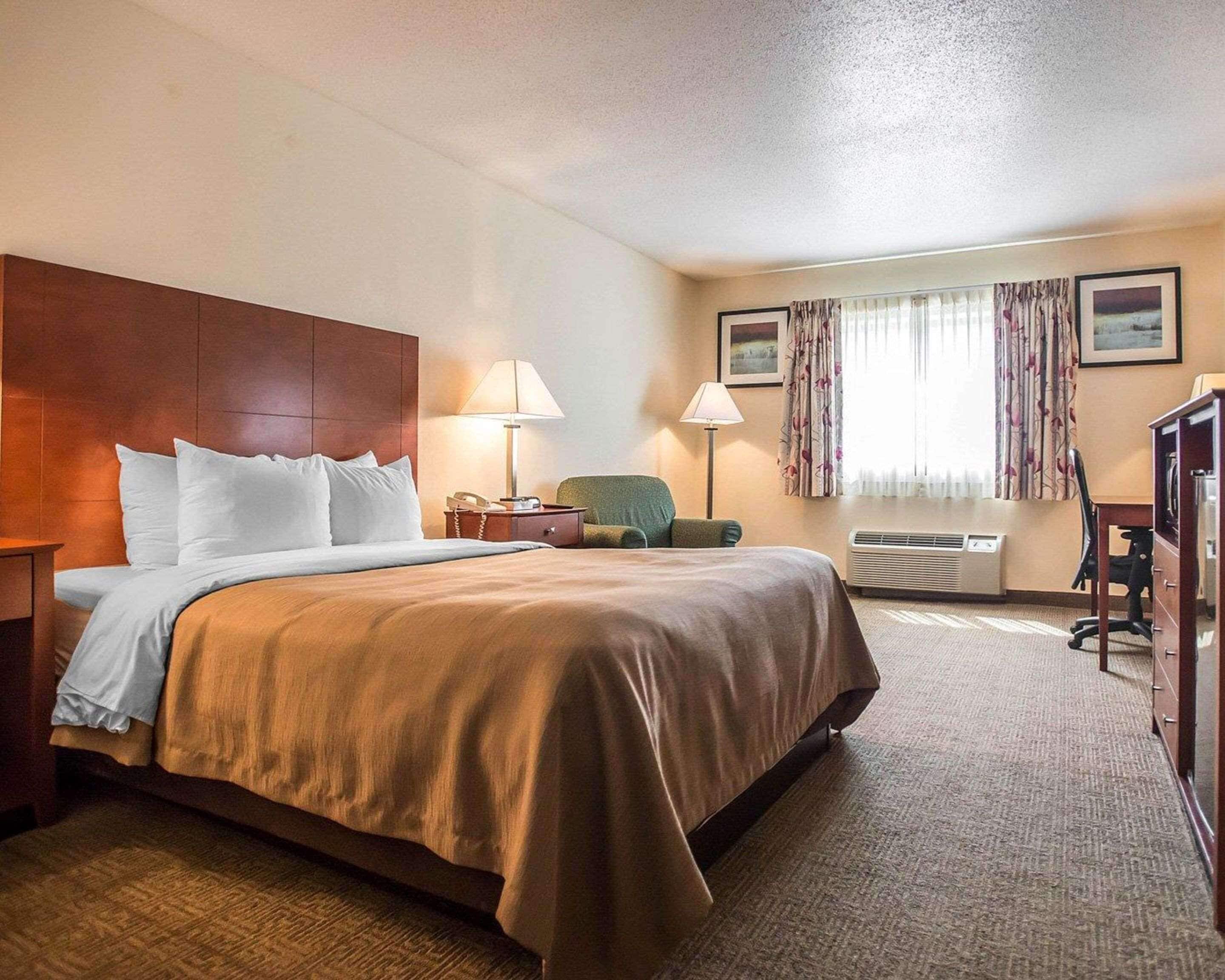 A hotel room with a large bed, a desk, a chair, a lamp, and a window with curtains.