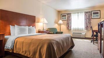 A hotel room with a large bed, a desk, a chair, a lamp, and a window with curtains.