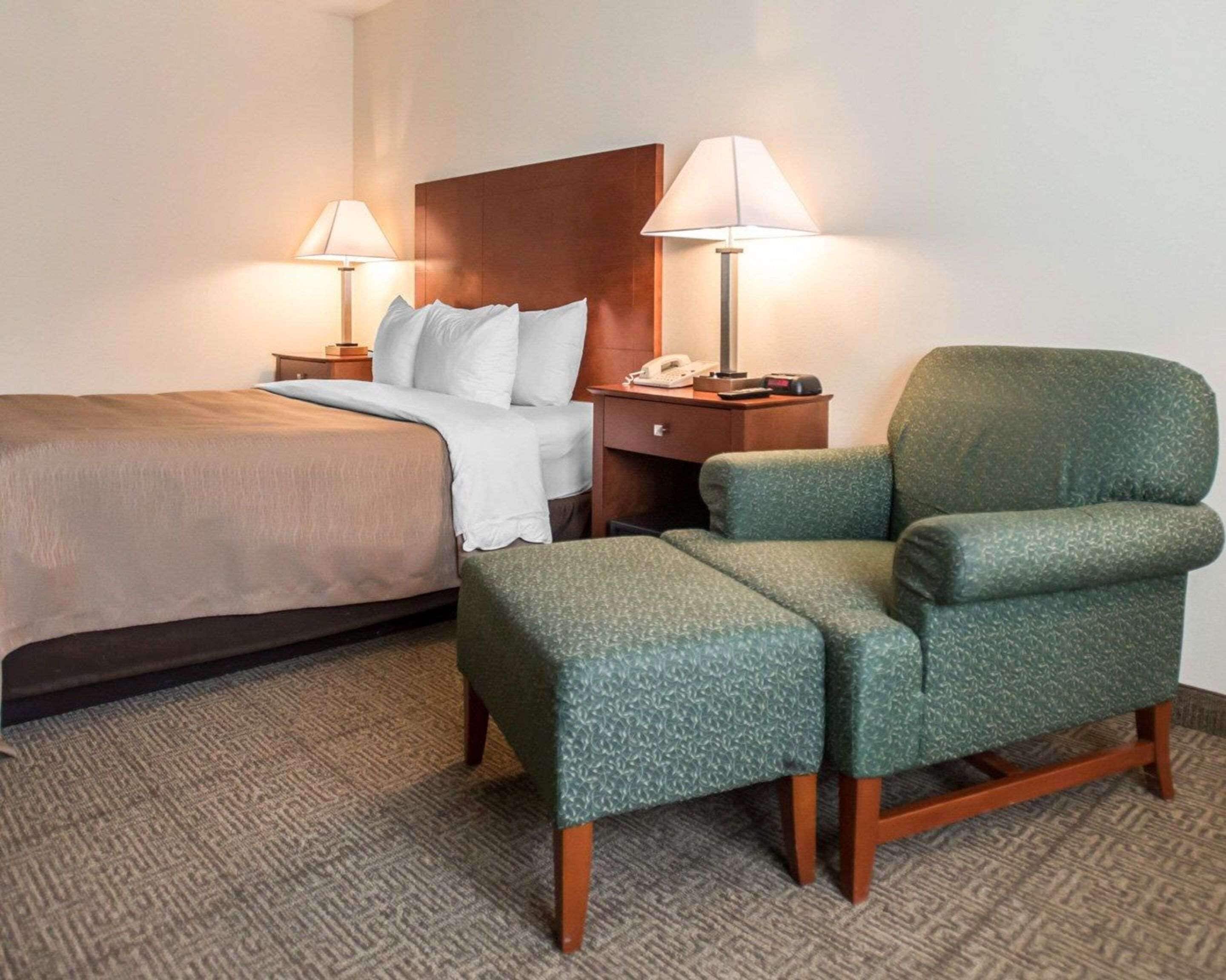Een hotelkamer met een bed, twee nachtkastjes met lampen, een groene fauteuil en een vloerbedekking.