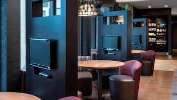 Un área de descanso moderna con diversas opciones de asiento, incluyendo mesas redondas y sillones acolchados, y televisores integrados.