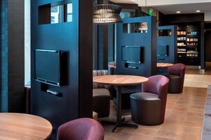 Un área de descanso moderna con diversas opciones de asiento, incluyendo mesas redondas y sillones acolchados, y televisores integrados.
