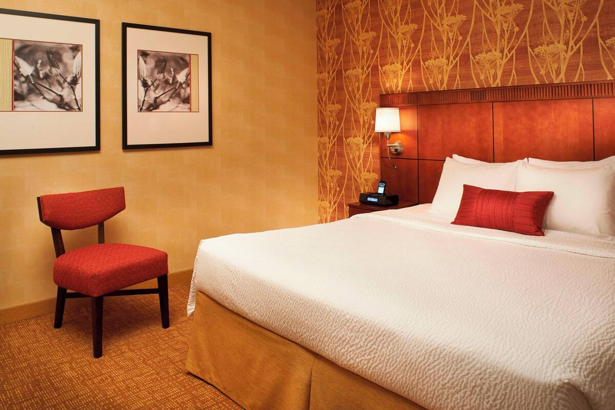 A hotel room with a large bed, a red chair, a nightstand with a lamp, and two framed pictures on the wall.