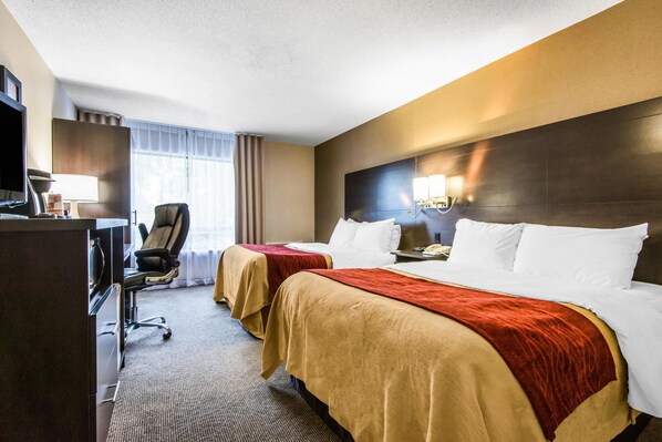 A hotel room with two beds, a desk, a chair, a TV, and a window with curtains.