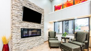 A modern living room with a stone wall, flat-screen TV, fireplace, comfortable seating, and large windows.