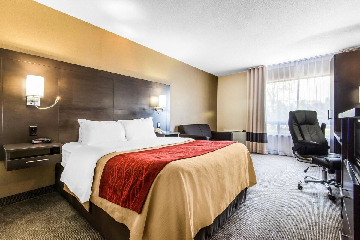 Une chambre d’hôtel comprenant un lit, des tables de chevet, un bureau, une chaise et une grande fenêtre avec des rideaux.