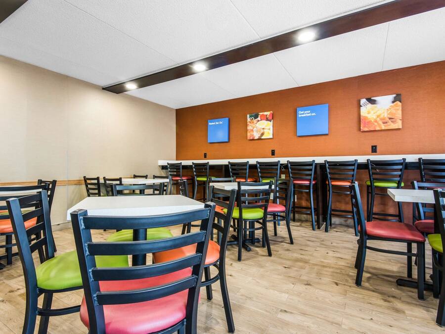 A cafeteria with multiple tables and chairs, featuring a variety of seating options and a wooden floor.