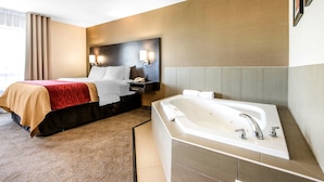 A hotel room with a large bed, a separate bathroom with a bathtub, and a nightstand with a lamp.