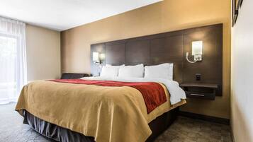 A hotel room with a large bed, a bedside table, a nightstand, and a wall-mounted lamp.