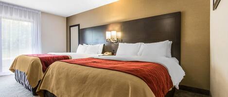 A hotel room with two beds, a large window with sheer curtains, a dark headboard, and a wall-mounted light fixture.