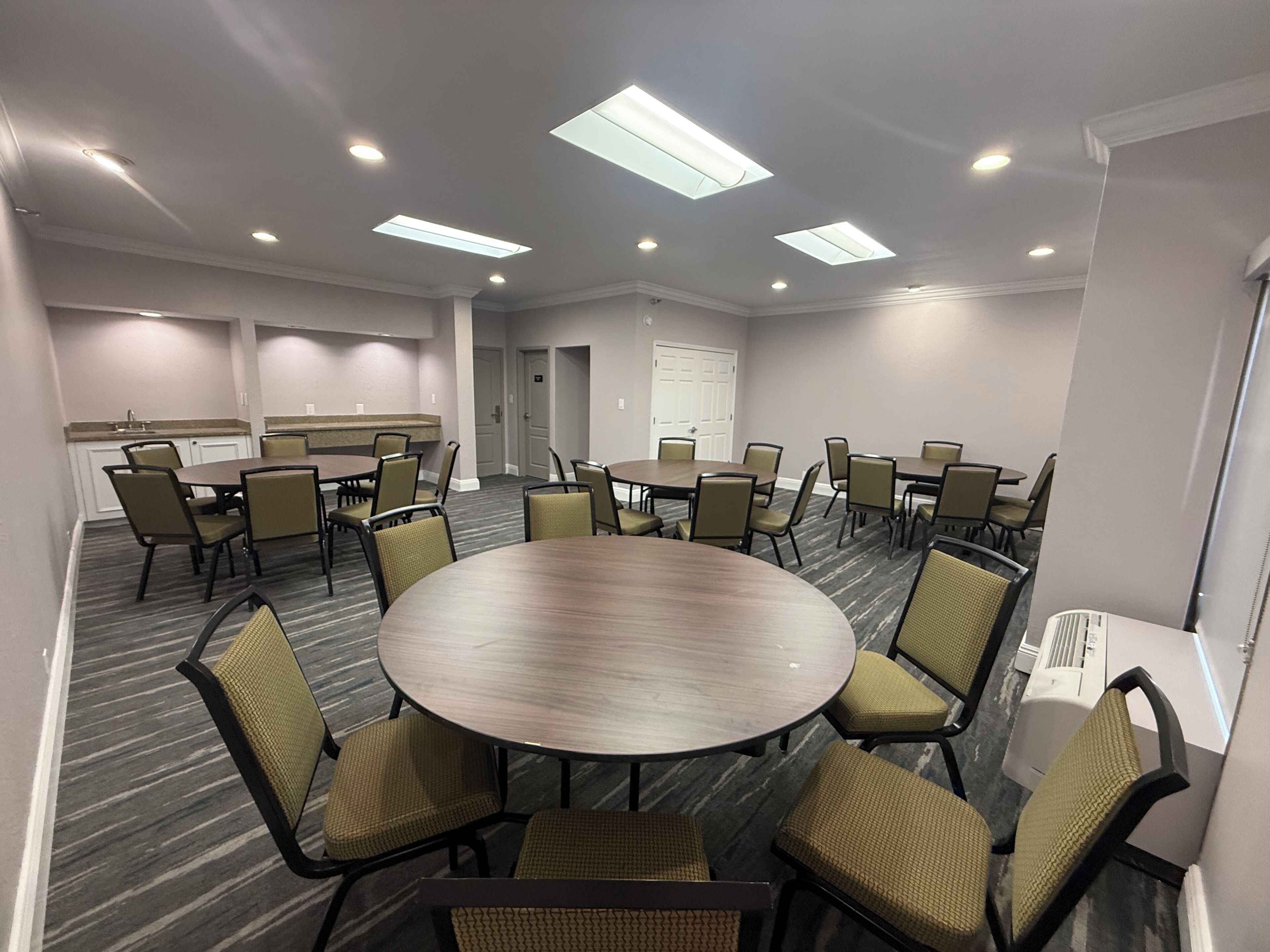 A conference room with a large round table, multiple chairs, and ceiling lights.