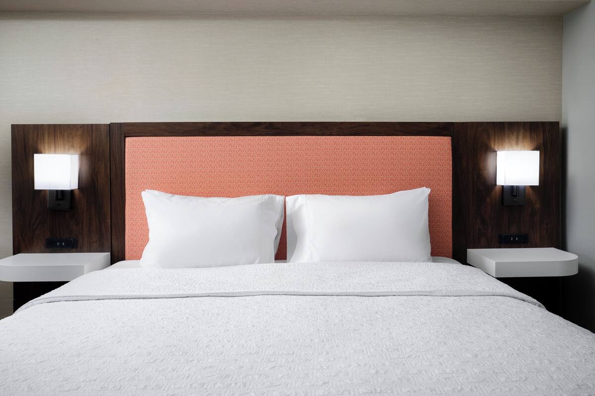 A hotel room with a large bed, two bedside tables, and a headboard with a textured design.