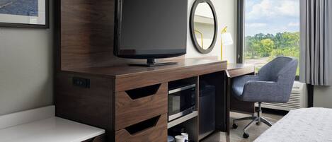 Une chambre d’hôtel équipée d’une télévision, d’un bureau, d’une chaise, d’un lit, d’une fenêtre avec des rideaux et d’un tableau encadré au mur.