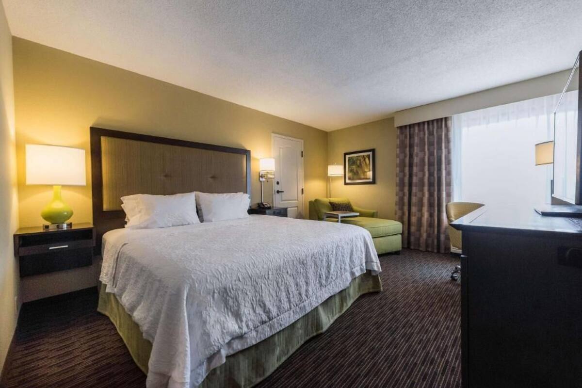 A hotel room with a large bed, bedside tables, a desk, a chair, and a window with curtains.