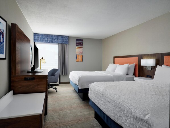 Une chambre d’hôtel avec deux lits, un bureau, une chaise et un téléviseur.