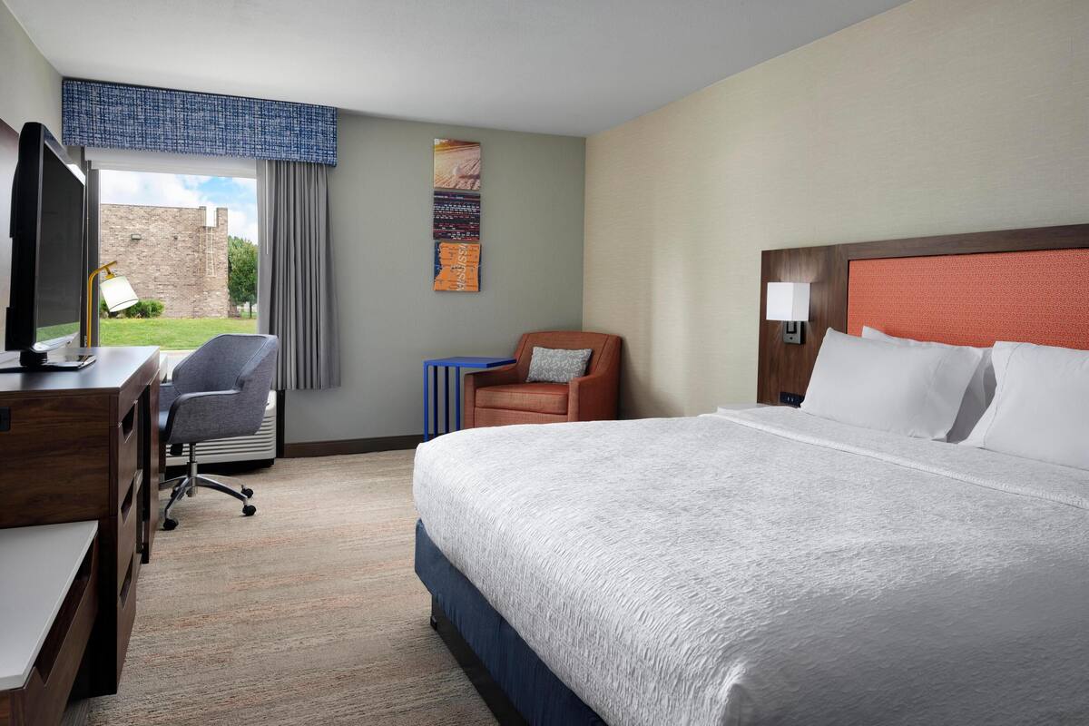 A hotel room with a large bed, a desk with a computer, a chair, and a view of the outdoors.