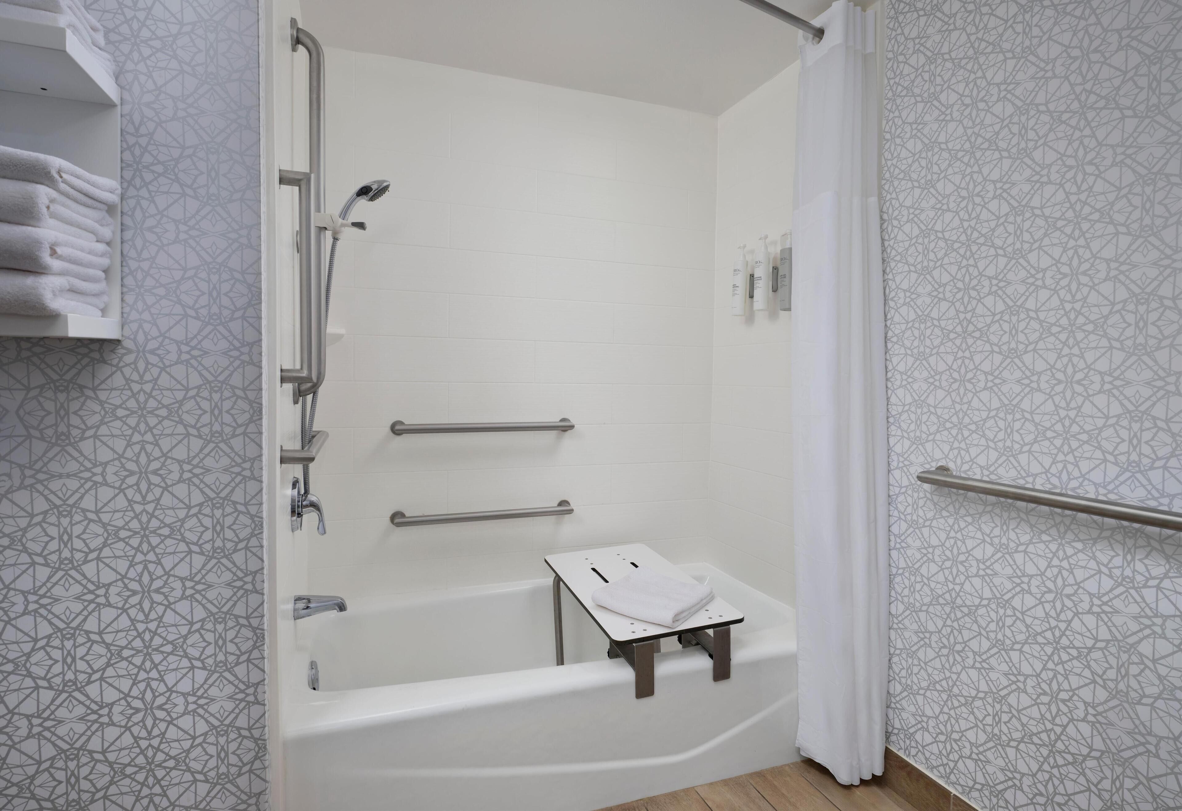 A modern bathroom with a walk-in shower, grab bars, a small bench, and a towel rack.