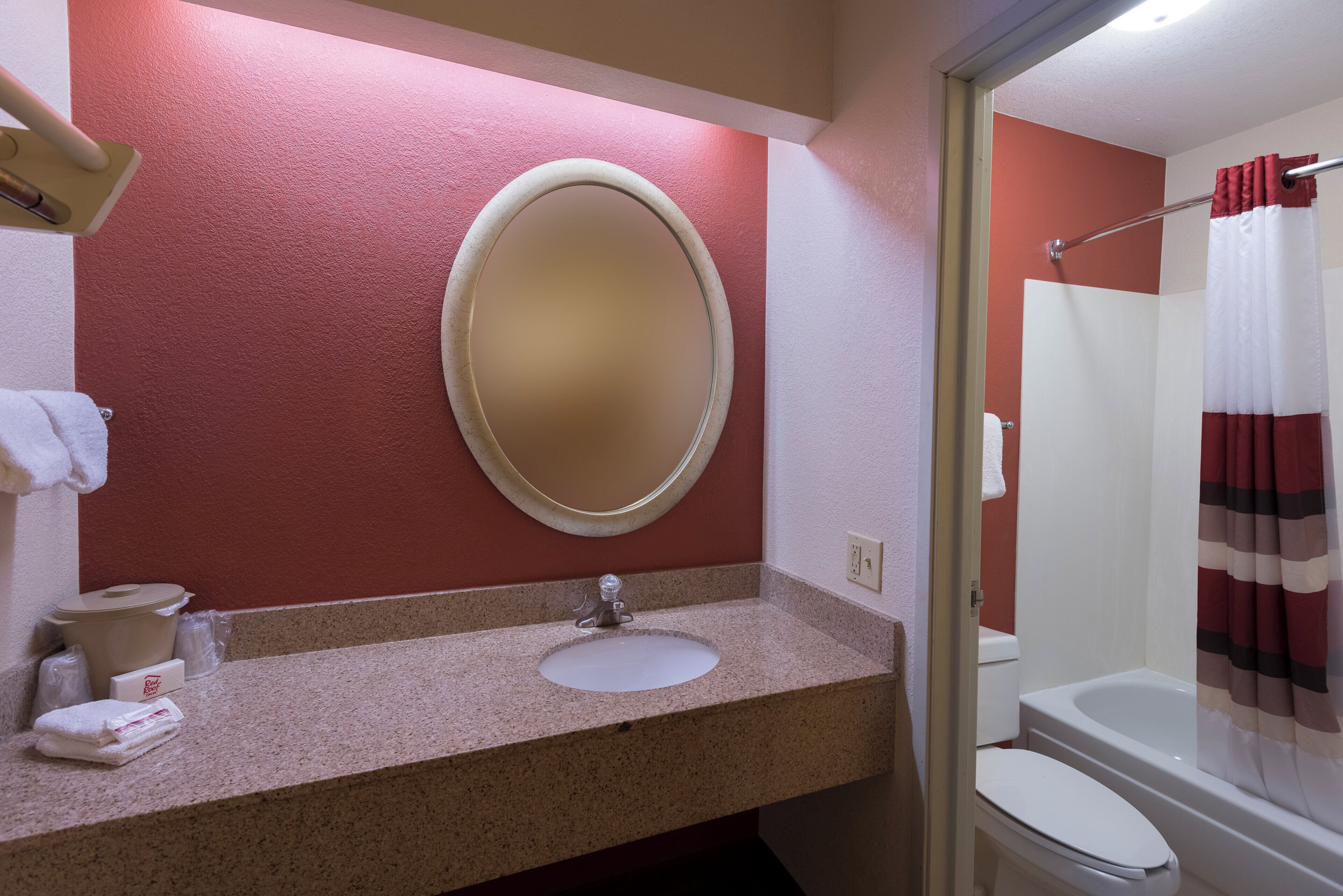 A bathroom with a granite countertop, a round mirror, a white sink, a toilet, and a shower curtain.