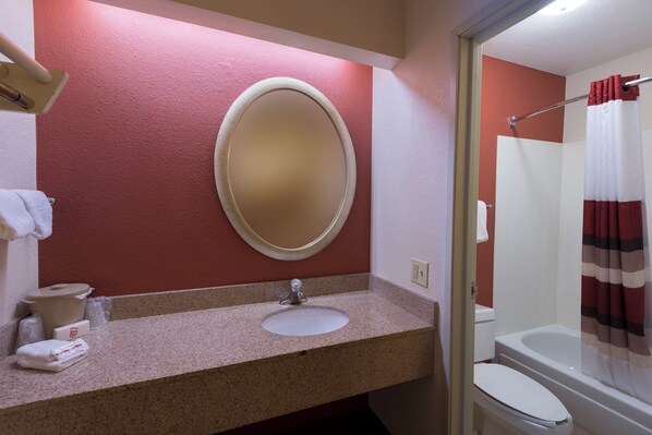 A bathroom with a granite countertop, a round mirror, a white sink, a toilet, and a shower curtain.