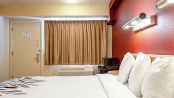 A hotel room with a bed, a television, a heater, and a door with a sign.