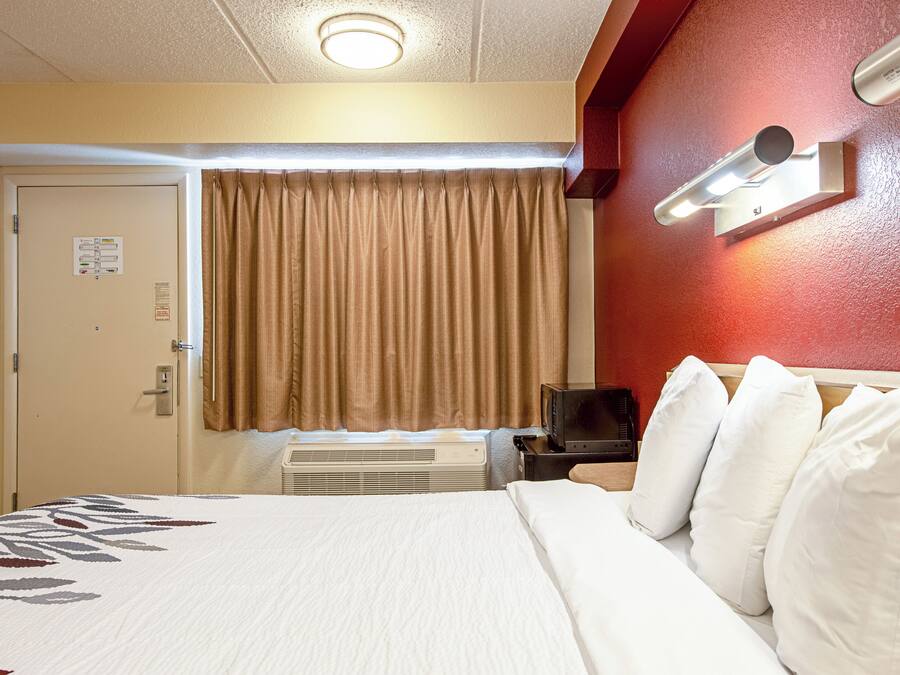 A hotel room with a bed, a television, a heater, and a door with a sign.