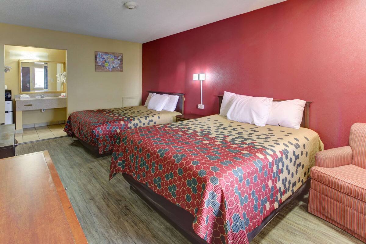 A hotel room with two beds, a desk, a chair, a mirror, and a nightstand.