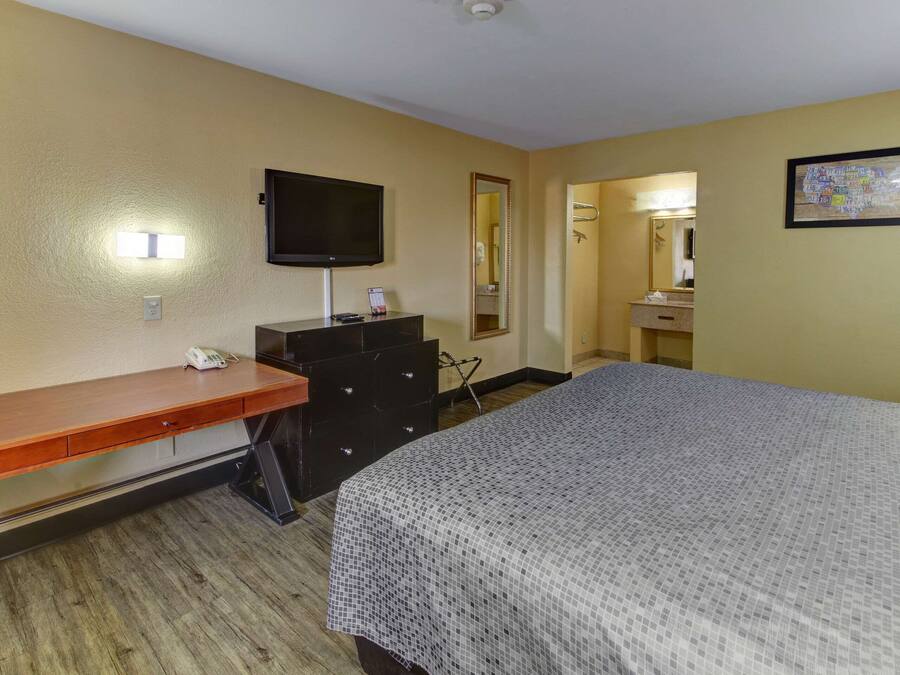 A hotel room with a bed, a desk, a dresser, a television, a mirror, and a bathroom visible through an open door.