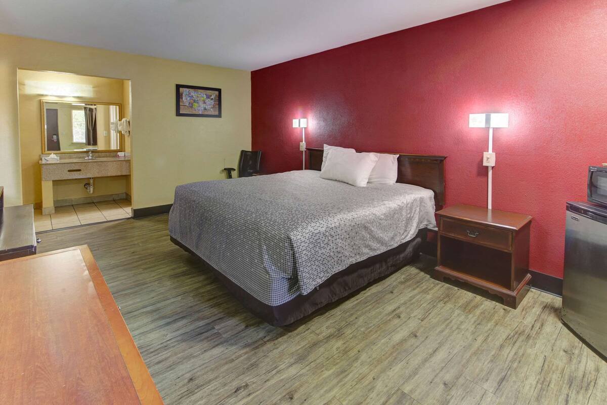 A hotel room with a bed, bedside tables, a desk, a mirror, and a red wall.