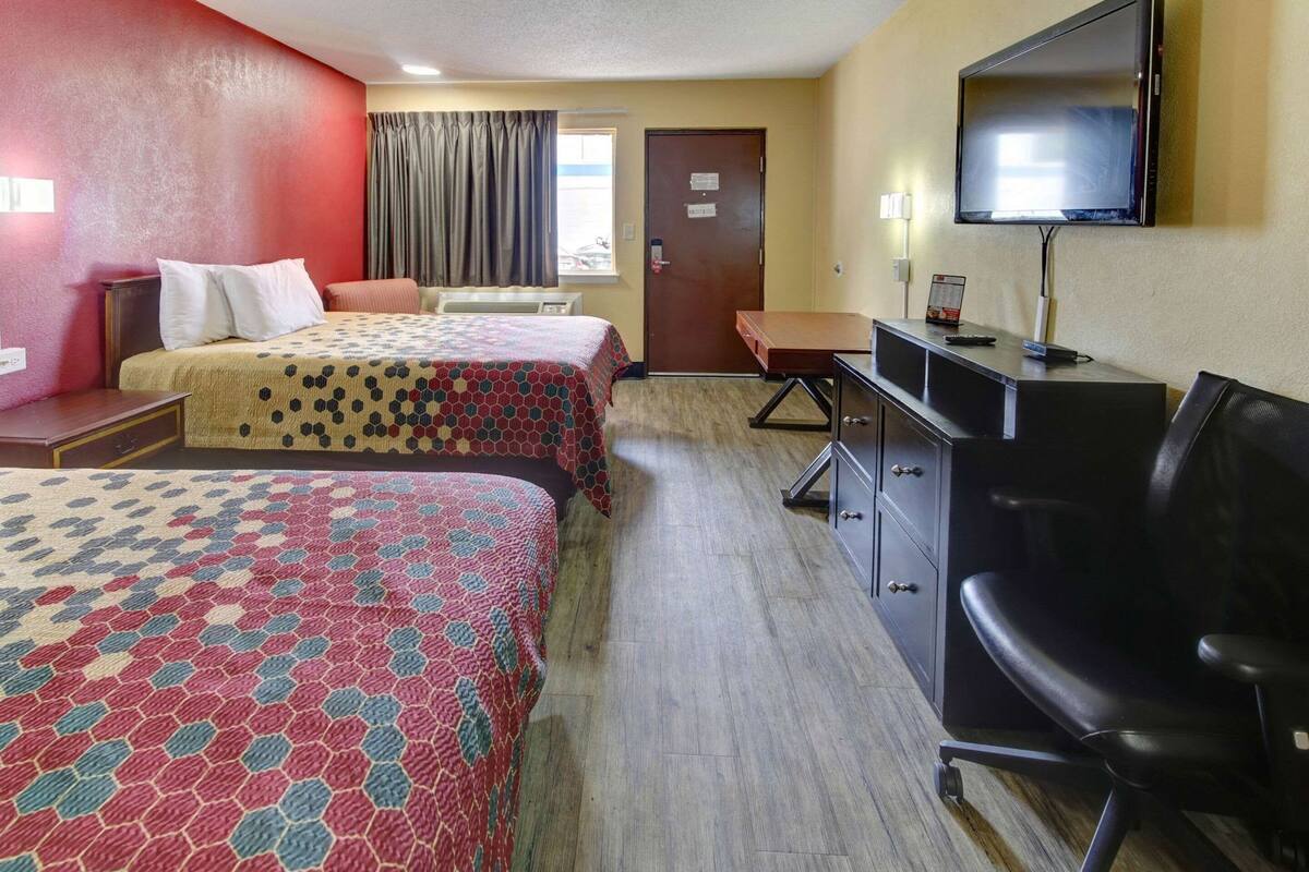 A hotel room with two beds, a desk, a chair, and a TV.